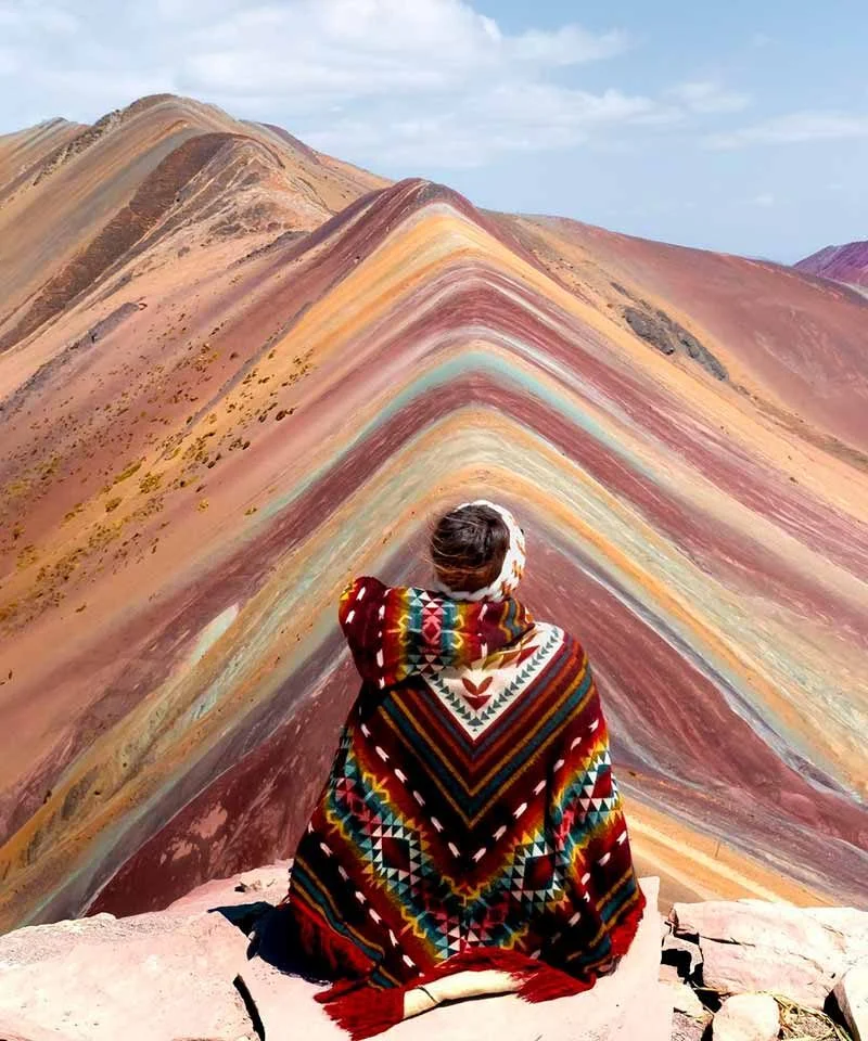 Turista com poncho andino admirando a montanha colorida